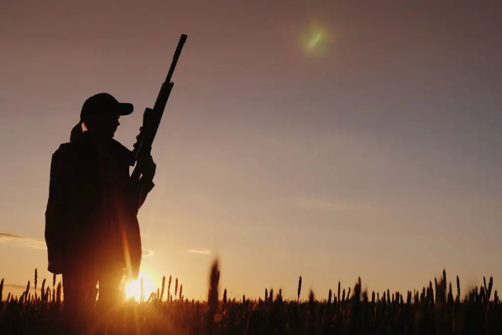 Woman hunting with a rifle at sunset