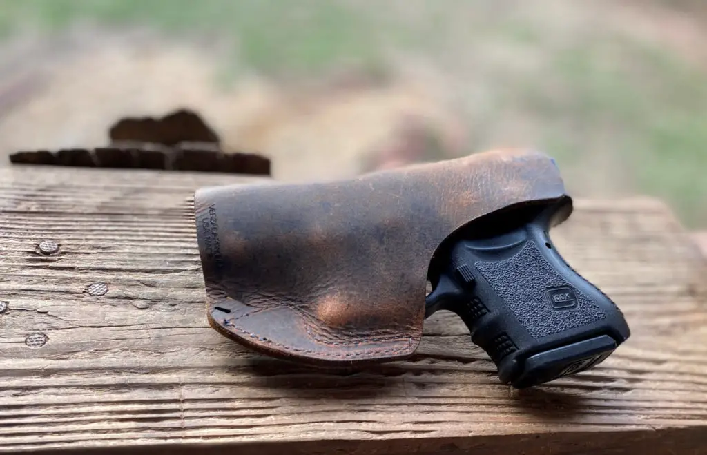 Glock 26 in leather holster sitting on wood table