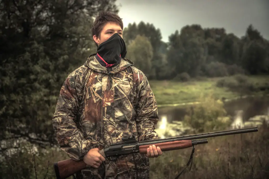 Man in camo coveralls holding a shotgun