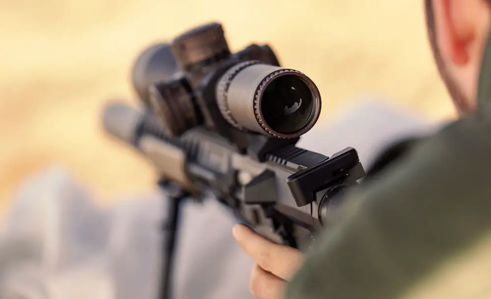 Man shooting rifle with a scope mounted on it looking into optic